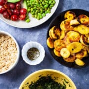 Cooked rice, tomatoes, sliced avocado, fried edamame beans, fried plantains, chimichurri sauce, and seasoning displayed on a table.