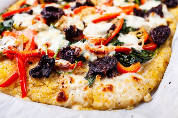 A close-up of a large vegetable polenta pizza topped with spinach, red bell pepper, sun dried tomatoes, onions, garlic, and mozzarella cheese.