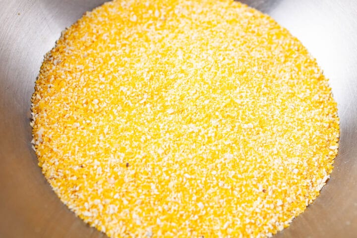 Yellow polenta (grains of cornmeal) in a stainless steel bowl.