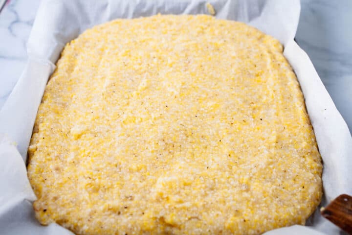 Cooked polenta placed on a prepared baking sheet and rectangular shaped as the base for a large pizza crust.