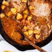 Cast iron skillet pork chops with apples, squash and pan juices served on a table.
