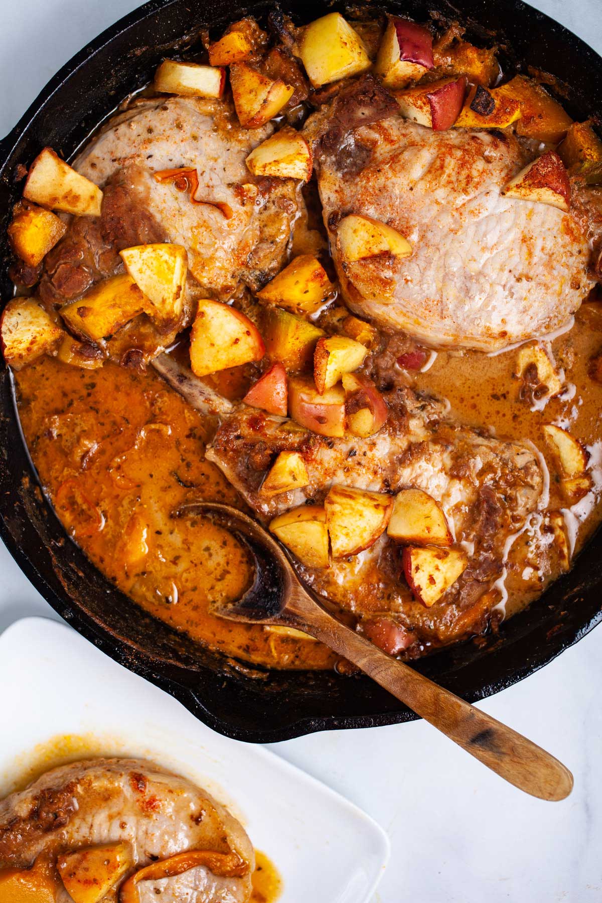 Cast iron skillet pork chops with apples, squash and pan juices served on a table.