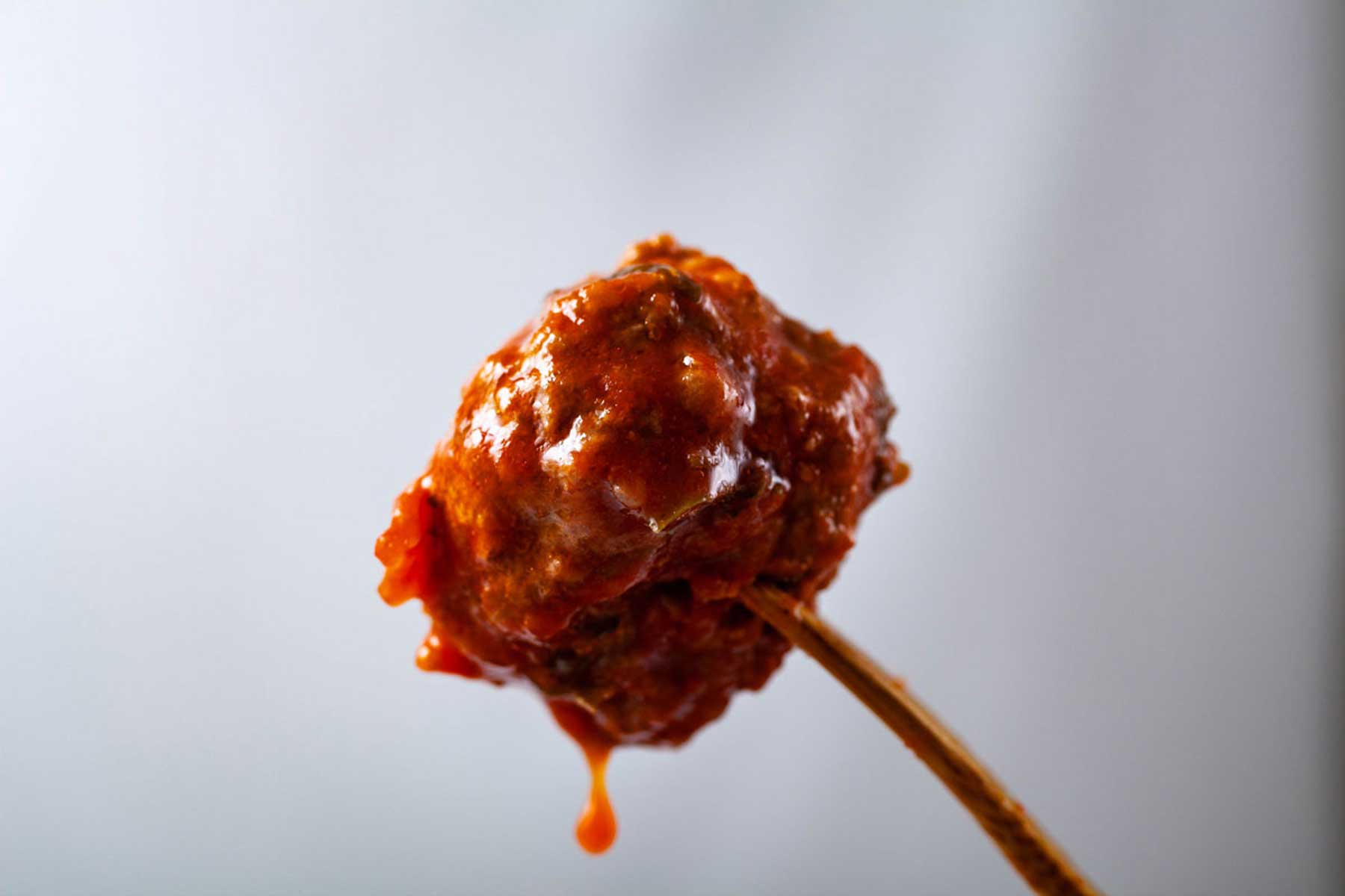 A wooden fork pierced into a juicy gluten-free meatball.