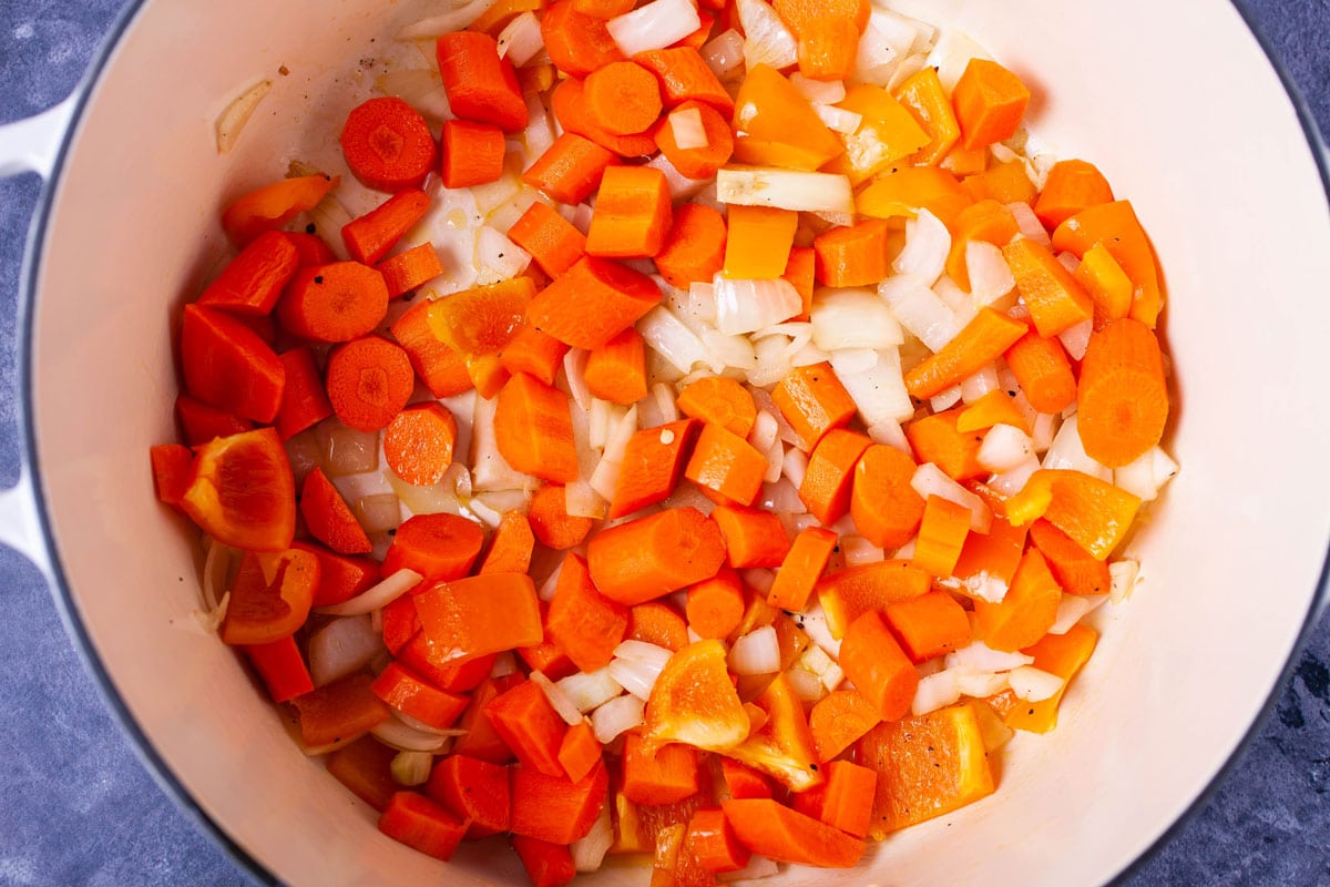 Chopped onions, orange bell pepper and carrots in a large pot.
