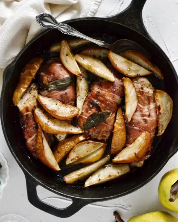 an overhead shot of prosciutto wrapped chicken surrounded by cooked pears in a cast iron skillet.