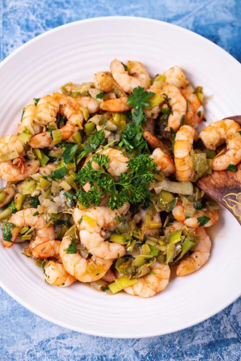 A large plate with spiced and garlicky shrimp and leeks plus fresh parsley garnish.