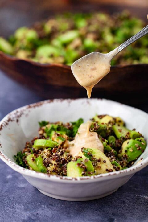 A teaspoon being lifted over a small salad bowl dropping salad dressing on top.