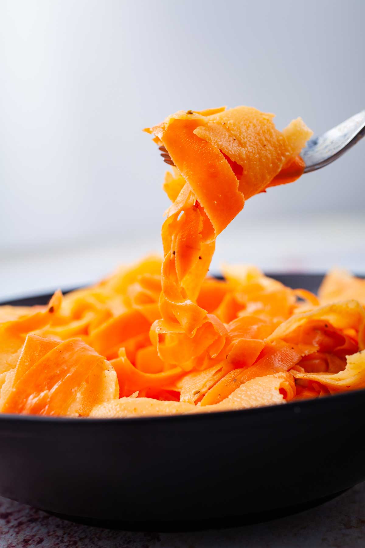 A fork holding a bite of shaved raw carrots and apples over a serving bowl.