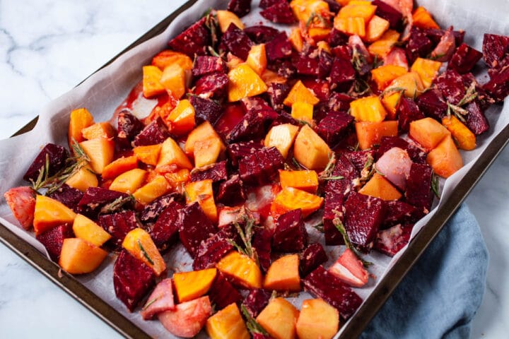 A large pan sheet with raw cubed beets, potatoes, and seasoned with herbs.