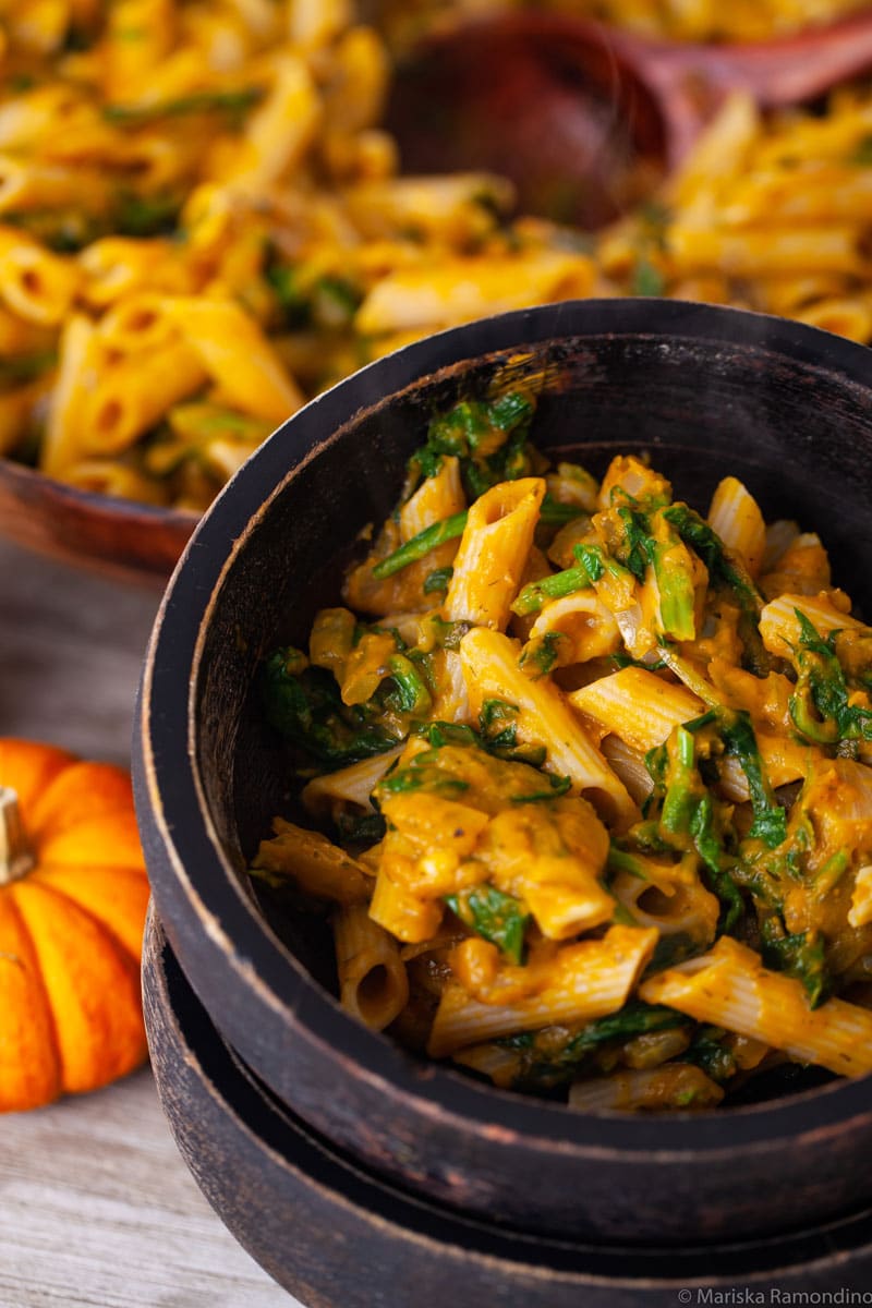 Two stacked wooden bowls with the bowl on top filled with a vegan pumpkin spinach pasta.