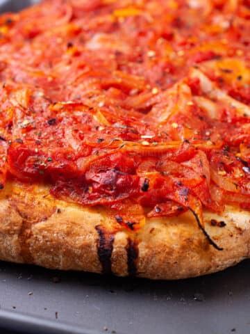 A thick crusted pizza with spicy red sauce onion toppings.