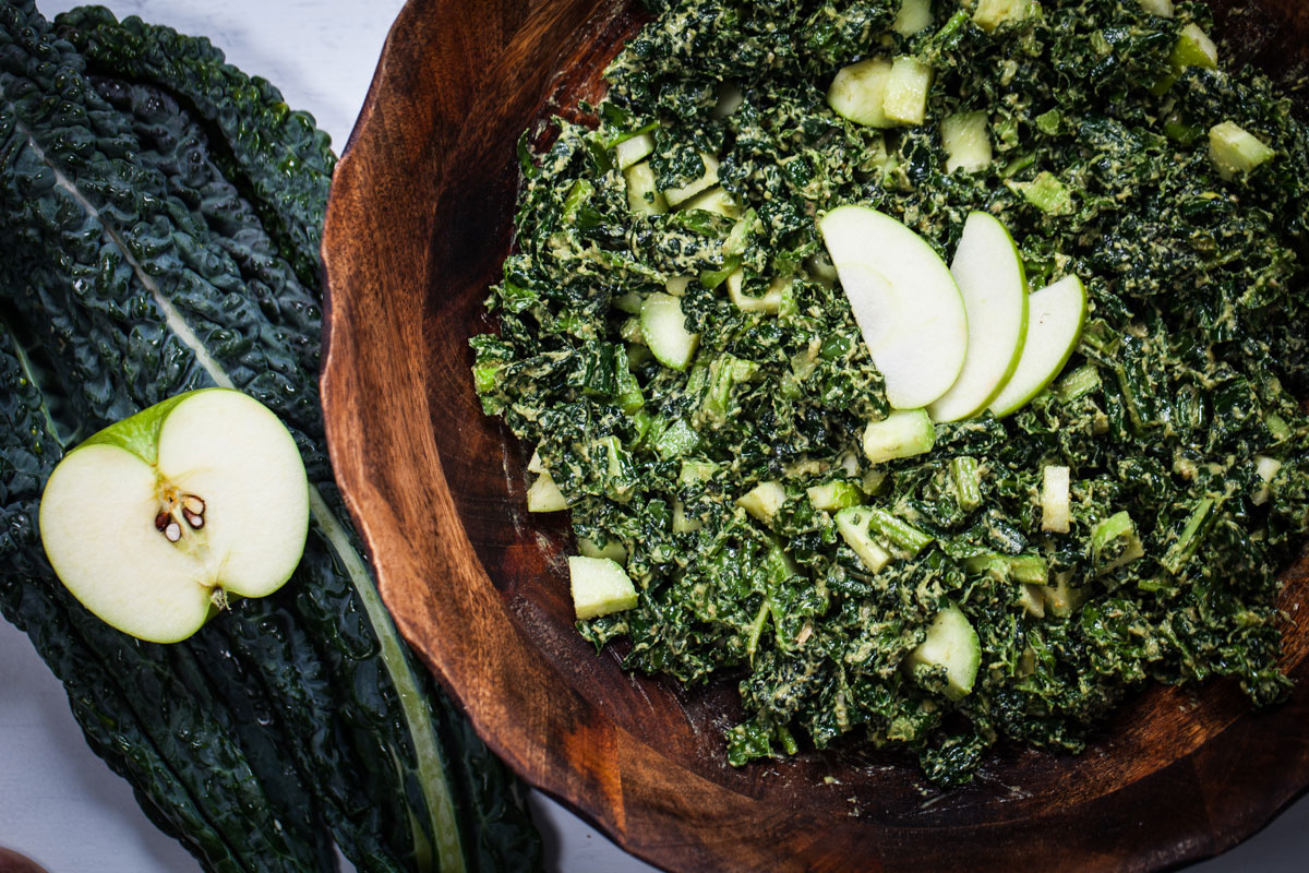A large bowl of creamy apple kale salad next to kale and apple ingredients