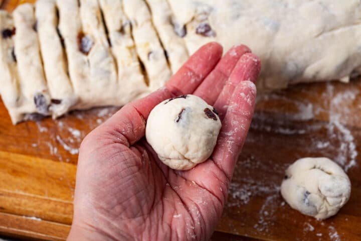 A hand holding a ball of raisin filled dough with the rest of the dough in the background.