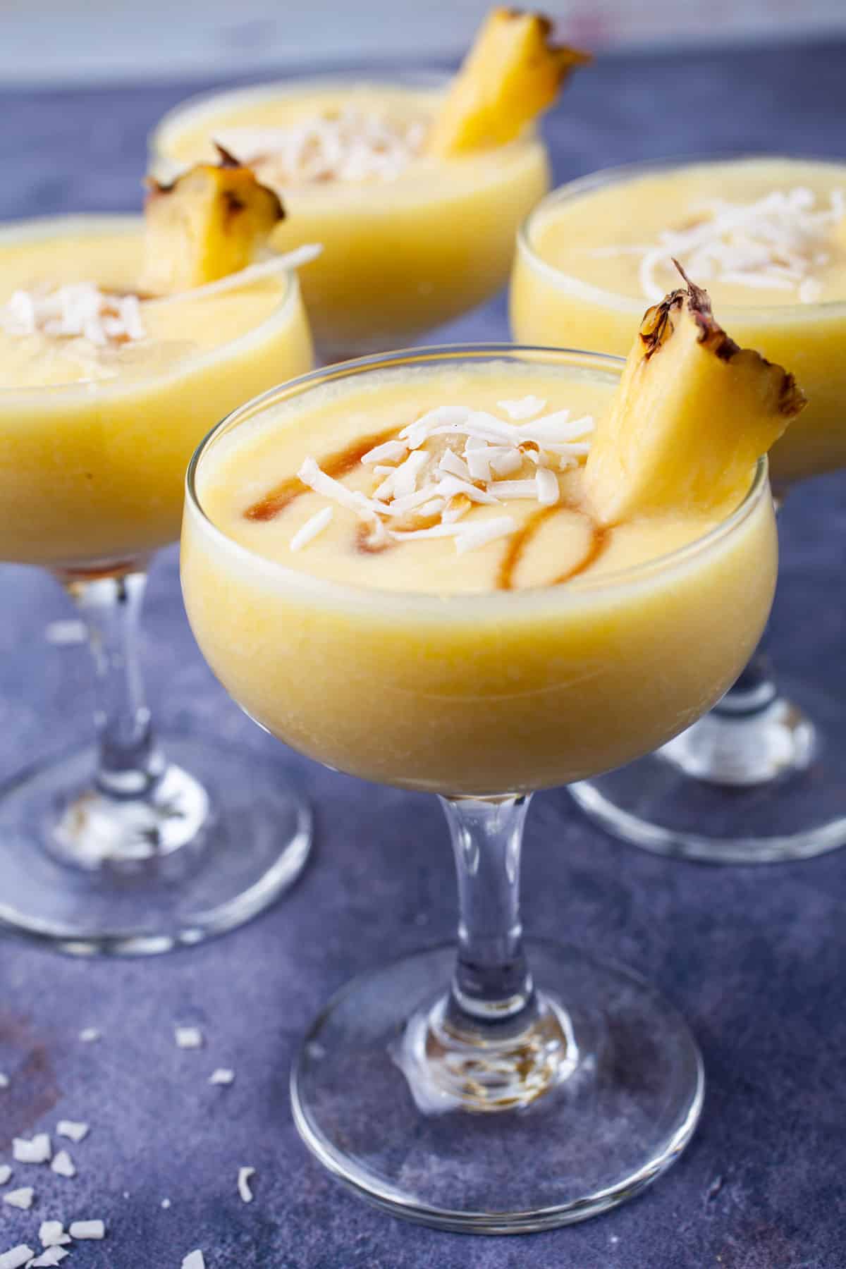 Pina colada mocktail drinks garnished with coconut shreds, a drizzle of maple syrup and fresh pineapple slices.