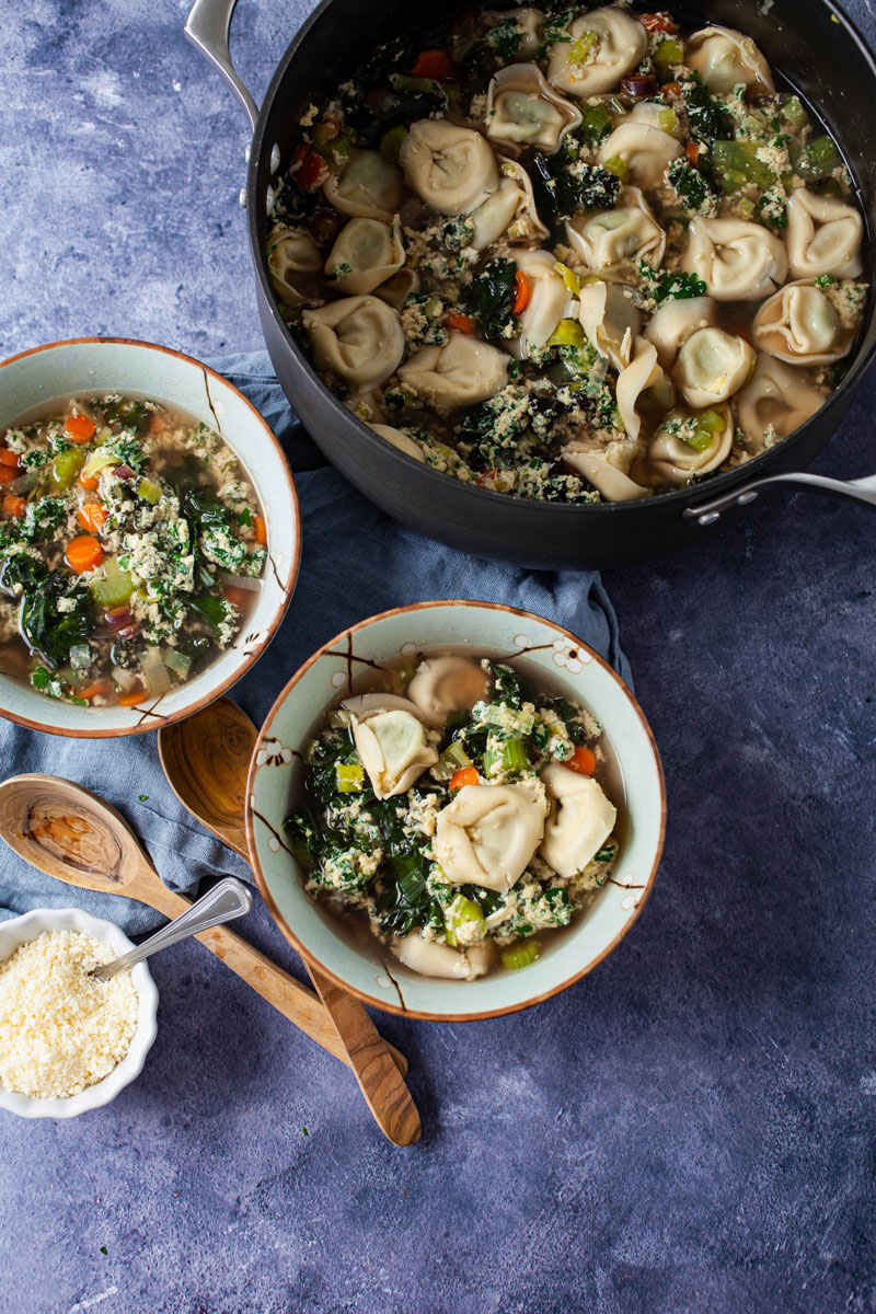 Two bowls filled with Straciatella soup next to a large pot of soup, extra Parmesan cheese and wooden spoons on the side.