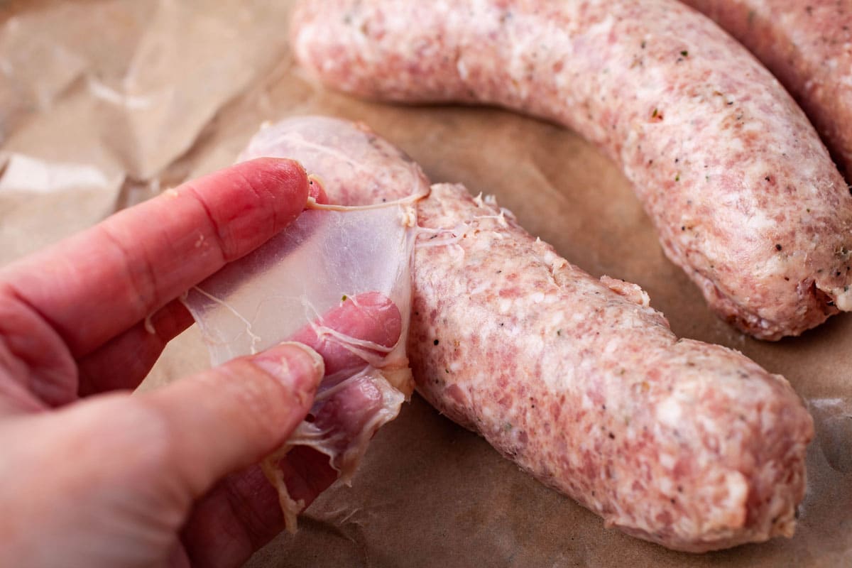 A hand tearing off the skin from a sausage.