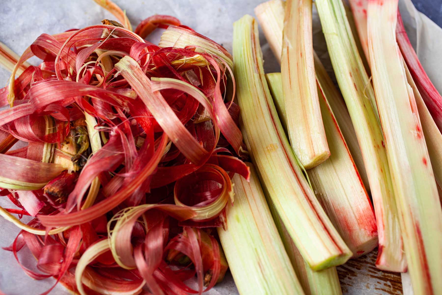 Peeled raw rhubarb stalks arranged next to its own peel.