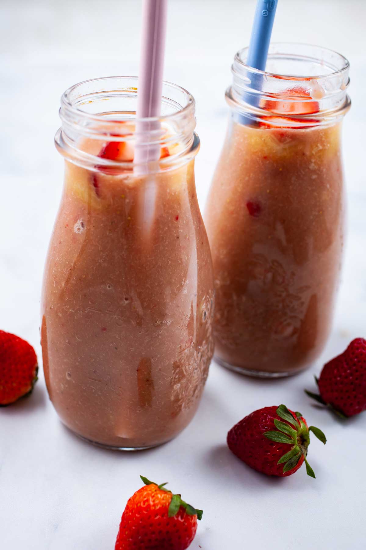 Two rhubarb smoothies in glass jars with straws.