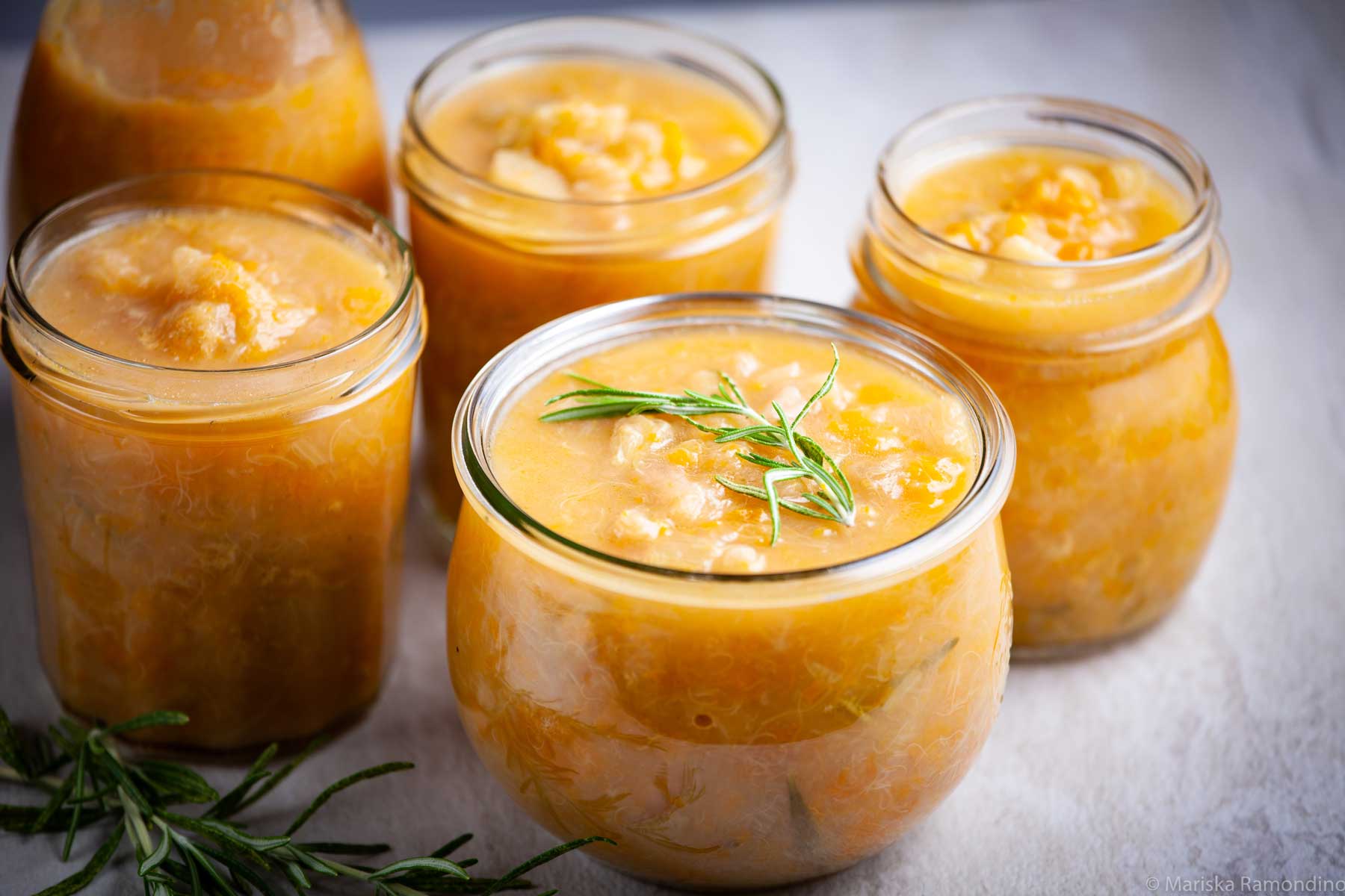 Small glass jars filled with rhubarb-apricots compote and garnished with fresh rosemary.