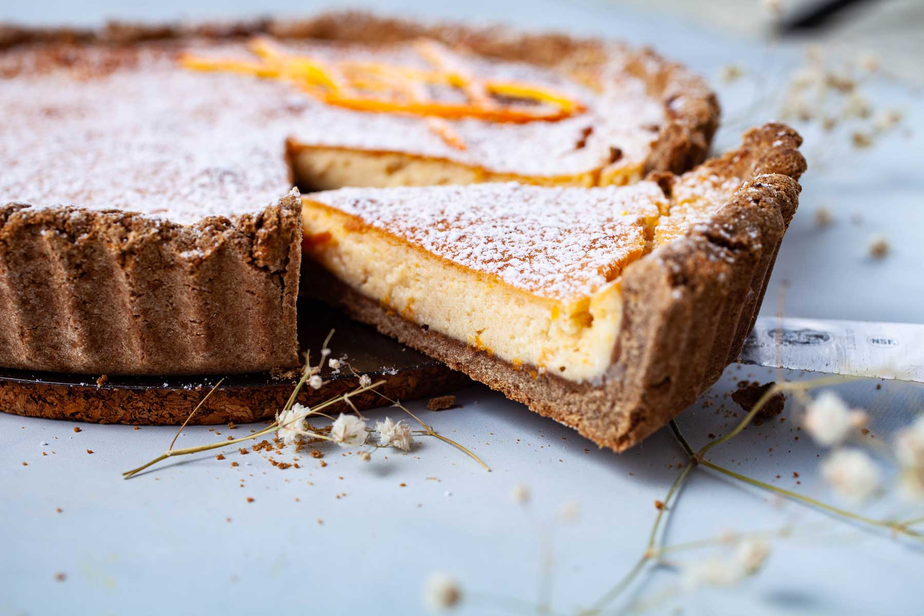 A piece of ricotta pie lifted up from a whole pie.