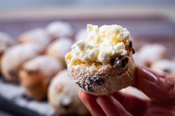 A hand holding half of an Italian and raisin filled doughnut topped with ricotta cheese.