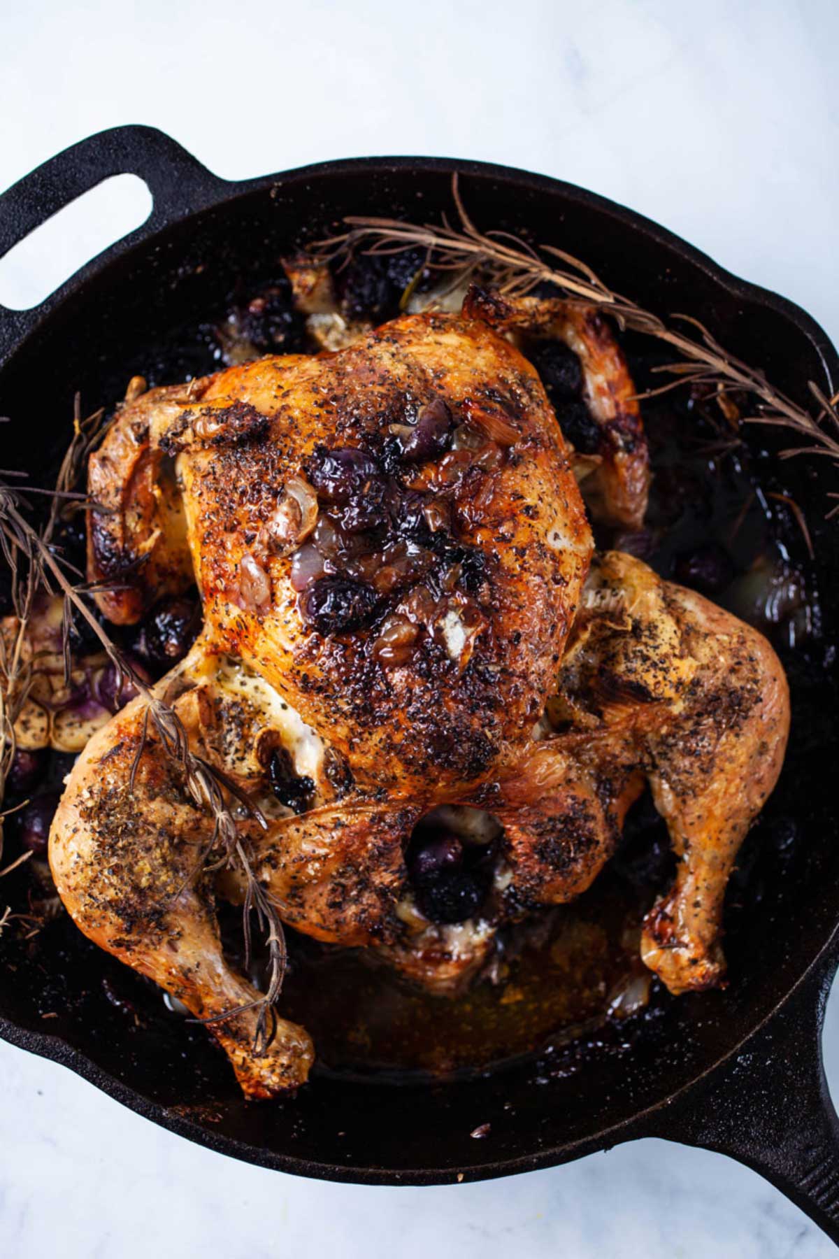 One whole roasted browned chicken in a cast-iron pan with pan juices.