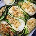 Baked baby bok choy topped with cheese served on a large white tray.