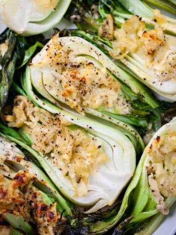 Baked baby bok choy topped with cheese served on a large white tray.