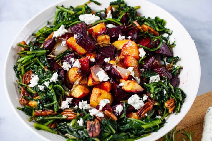 A large plate filled with roasted beets, potatoes, sauteed dandelion greens, pecans, topped with goat cheese.