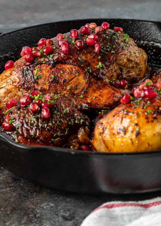 chicken in a cast iron pan topped with pomegranate and fresh herbs.