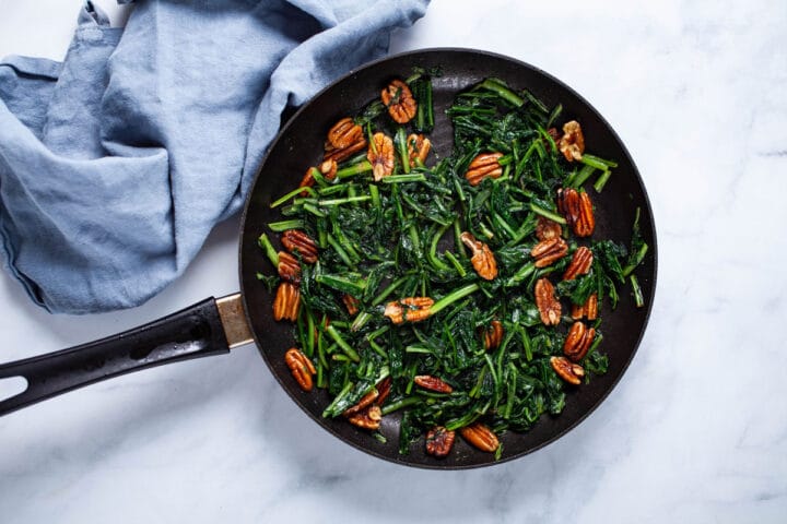 A medium-sized pan, filled with sauteed dandelion greens and pecans.