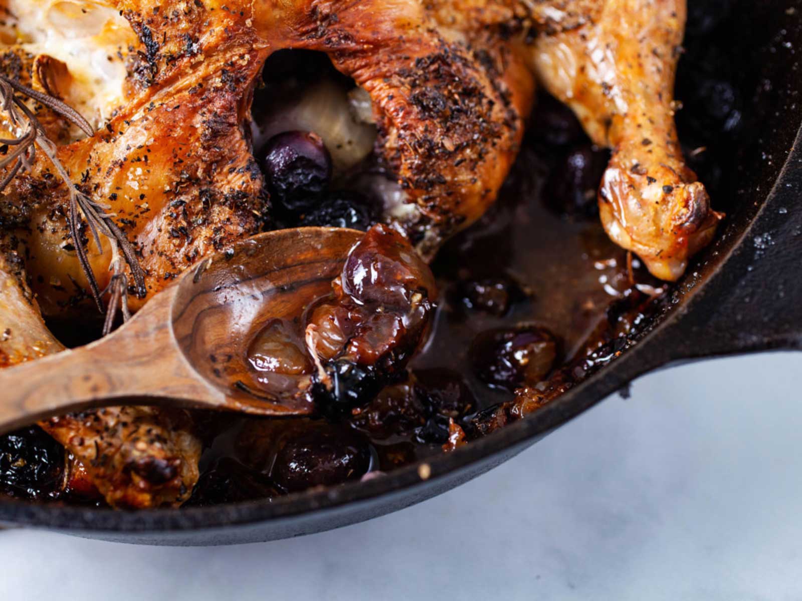 A spoon filled with pan juices from a roasted chicken resting on a cast-iron pan.