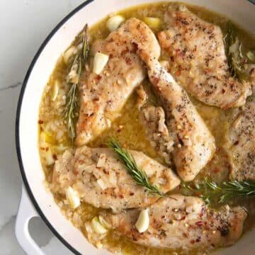 Baked chicken cutlets dunked in a sauce and presented in a Dutch oven pan.