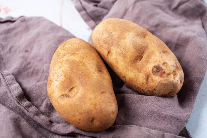 Two russet potatoes resting on a brown kitchen towel.