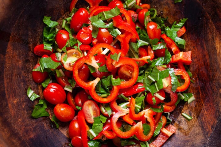 A salad with tomatoes, red bell pepper, and dandelion greens in a wooden bowl.