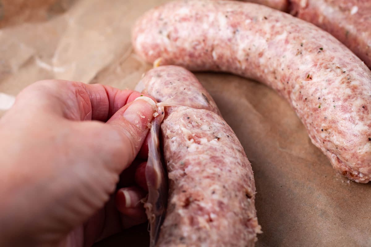 A hand tearing off the skin from a sausage.