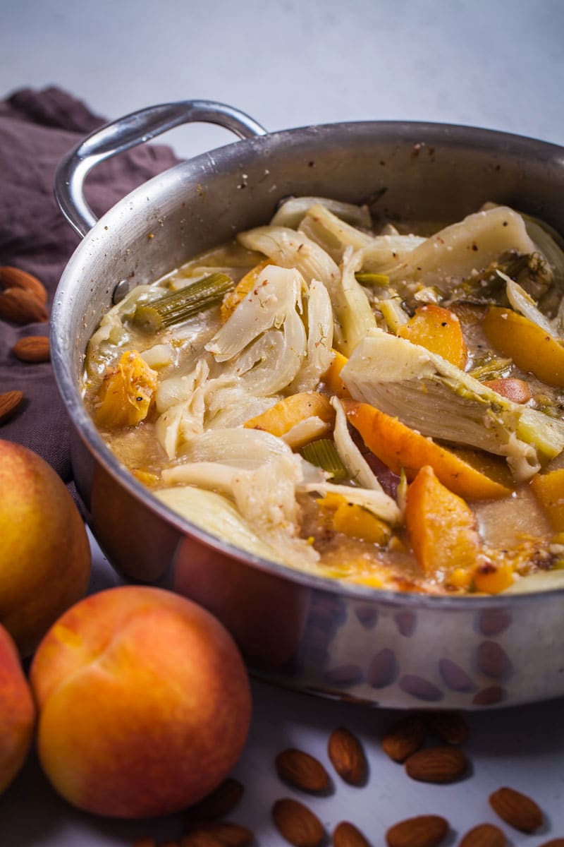 Soft braised fennel pieces and peaches in a creamy liquid in a large pan.