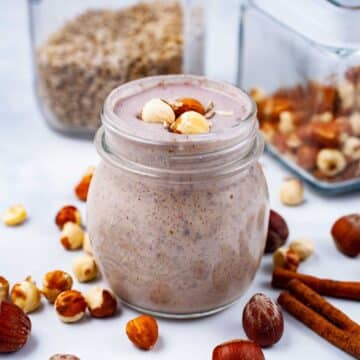 A creamy nut smoothie on a table, garnished with hazelnuts.