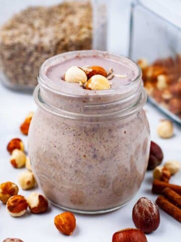 A creamy nut smoothie on a table, garnished with hazelnuts.
