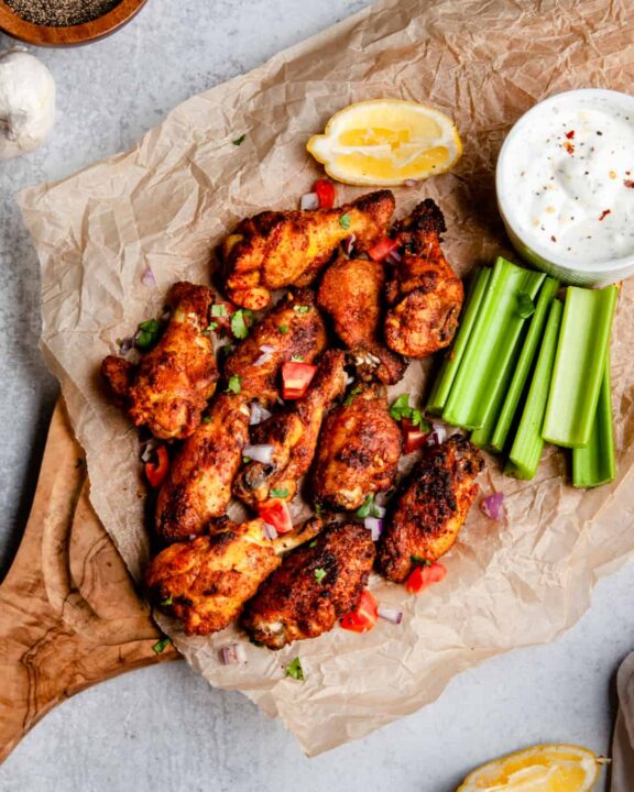 an overhead shot of shawarma spiced chicken wings on parchment paper on a cutting board beside celery slices and a dipping sauce.