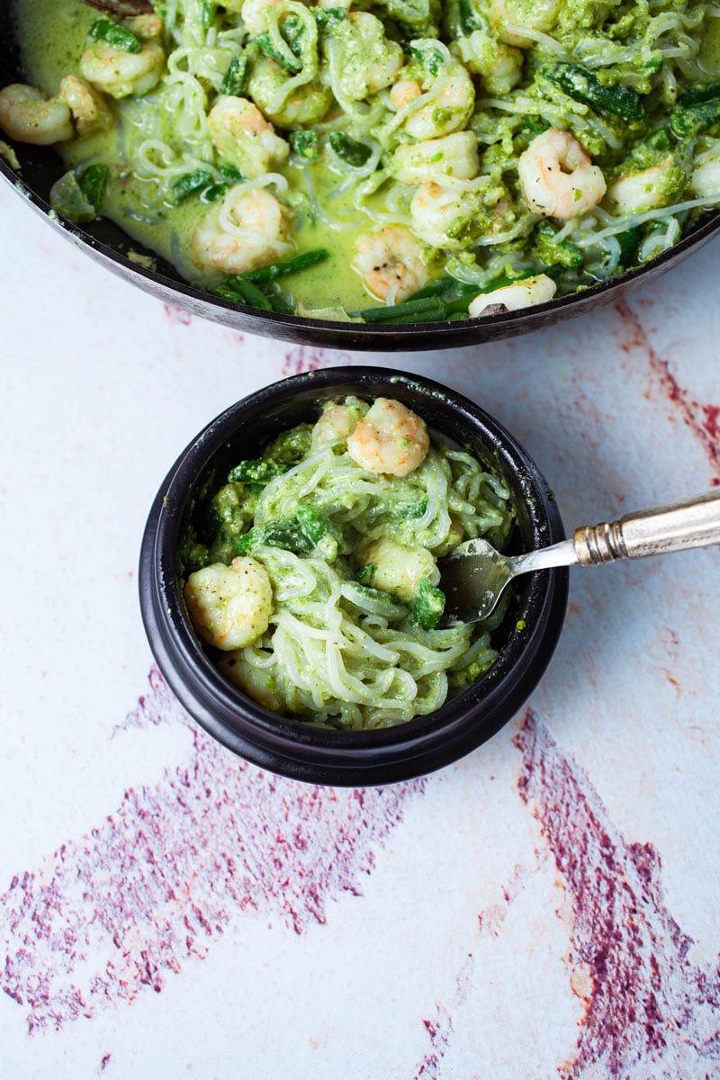 A fork resting in a bowl of Shirataki pasta with shrimp and pesto sauce.