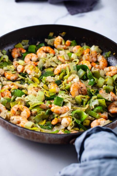 A closeup of a large skillet filled with sauteed shrimp and leeks.