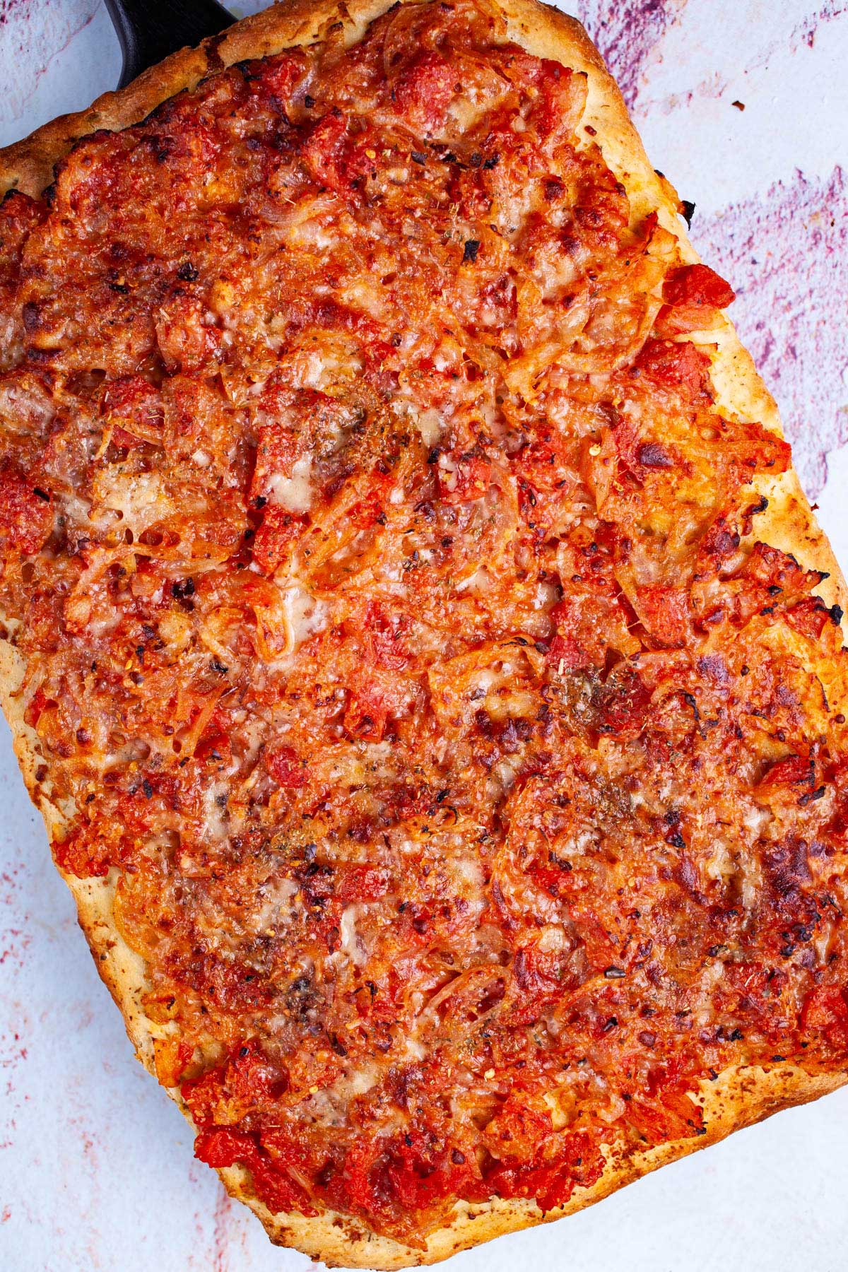 Thick-crust Sicilian pizza with onion-based toppings on a cutting board.