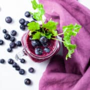 A glass of beet juice smoothie topped with blueberries and garnished with fresh cilantro leaves.