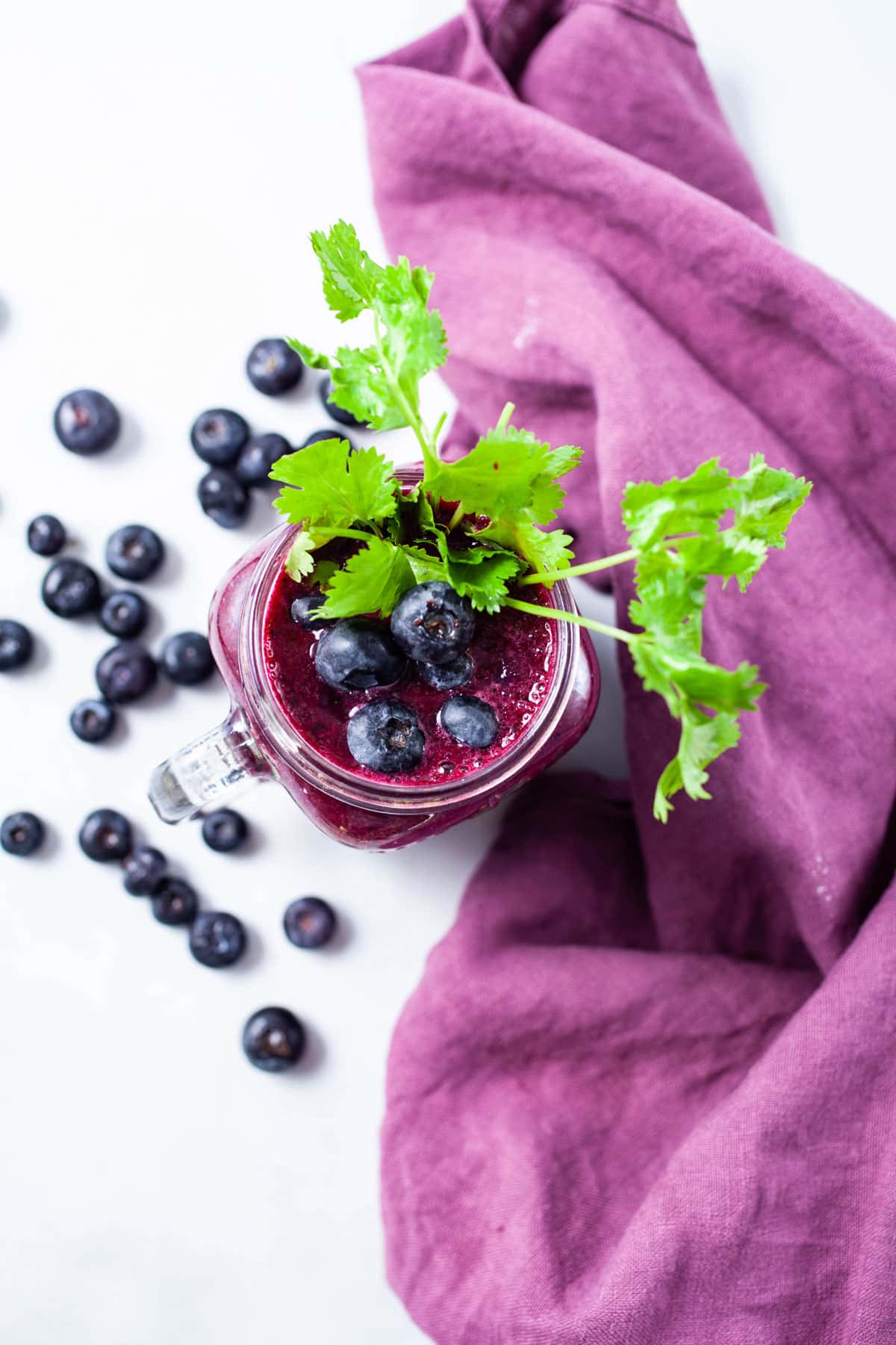 A glass of beet juice smoothie topped with blueberries and garnished with fresh cilantro leaves.