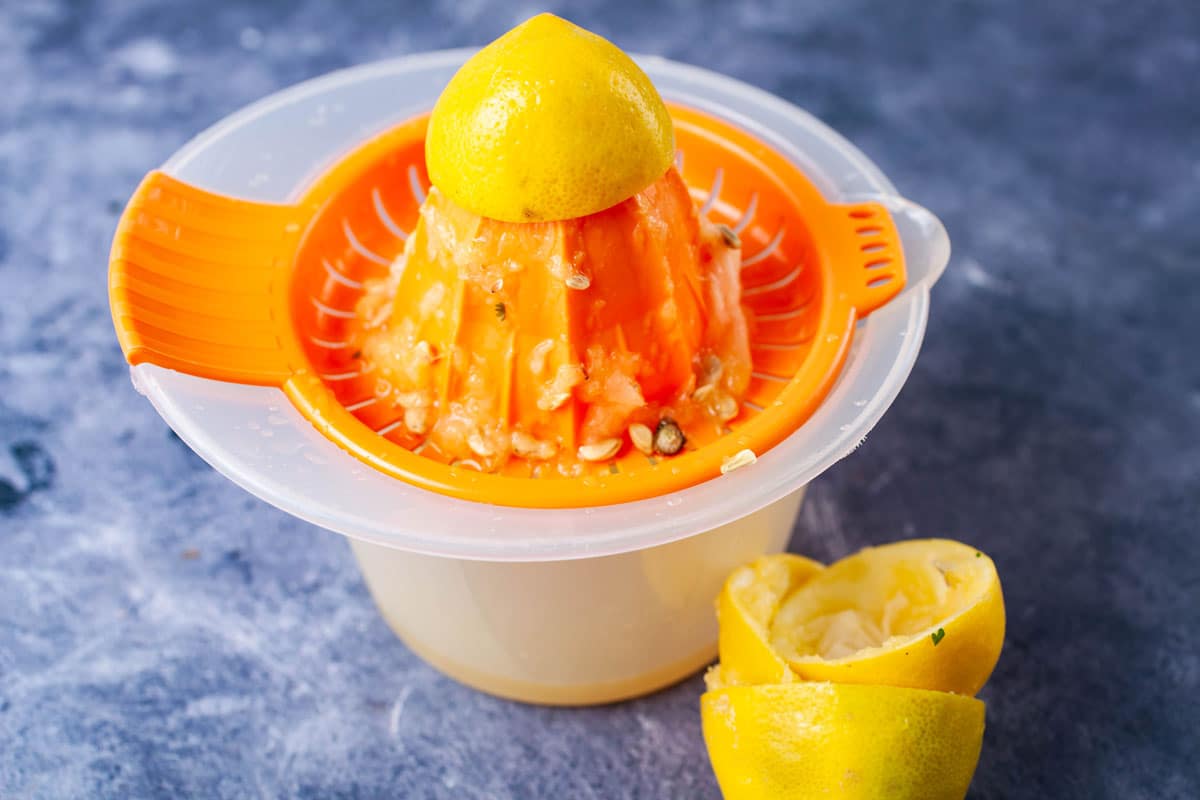 Half a juiced lemon on top of a hand juicer next to other stacked half lemon peels.