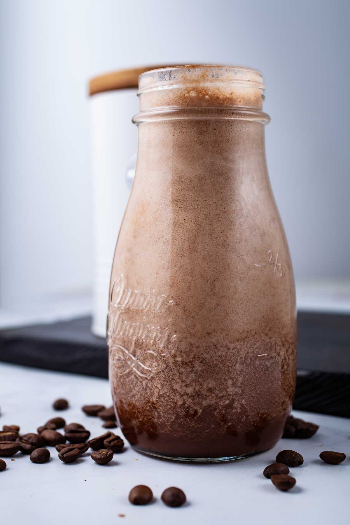 A coffee date smoothie in a small glass jar surrounded by coffee beans and oat snacks.