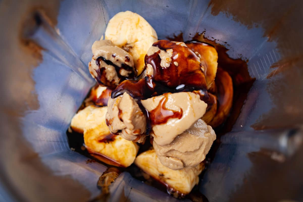 Chopped plantain, molasses, and tahini butter stacked on top of each other in a blender.