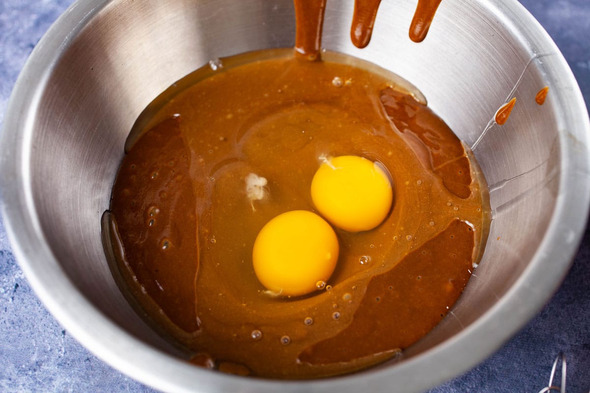 Two raw eggs resting on a brown batter in a stainless steel bowl.