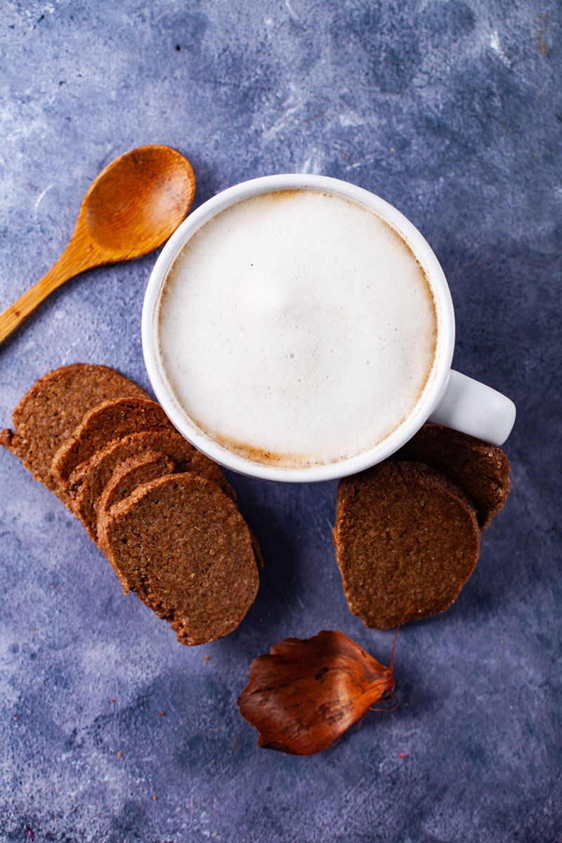 Homemade Biscoff Cookies stacked around a cup of latte and next to a wooden spoon.